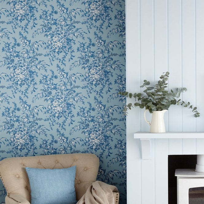 Laura Ashley wallpaper next to a paneled fireplace with plant on and behind an armchair. 