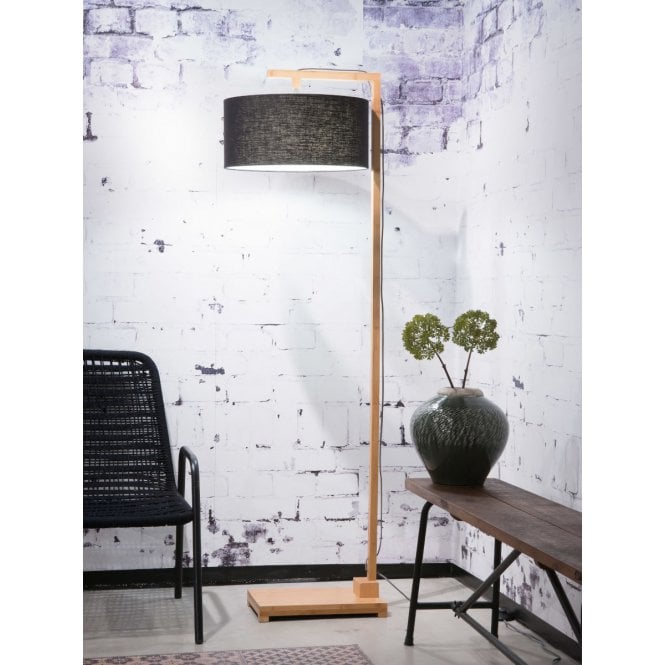 Floor lamp against a white bricked background next to a chair and bench.