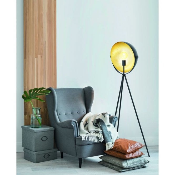A floor lamp next to an arm chair with a throw and set of cushions stacked on the floor.