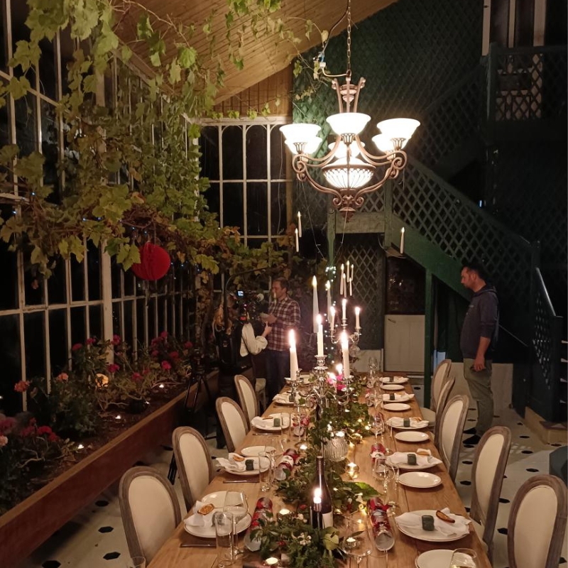 a large dining table in French chateau orangery with large, period chandelier adding a warm glow