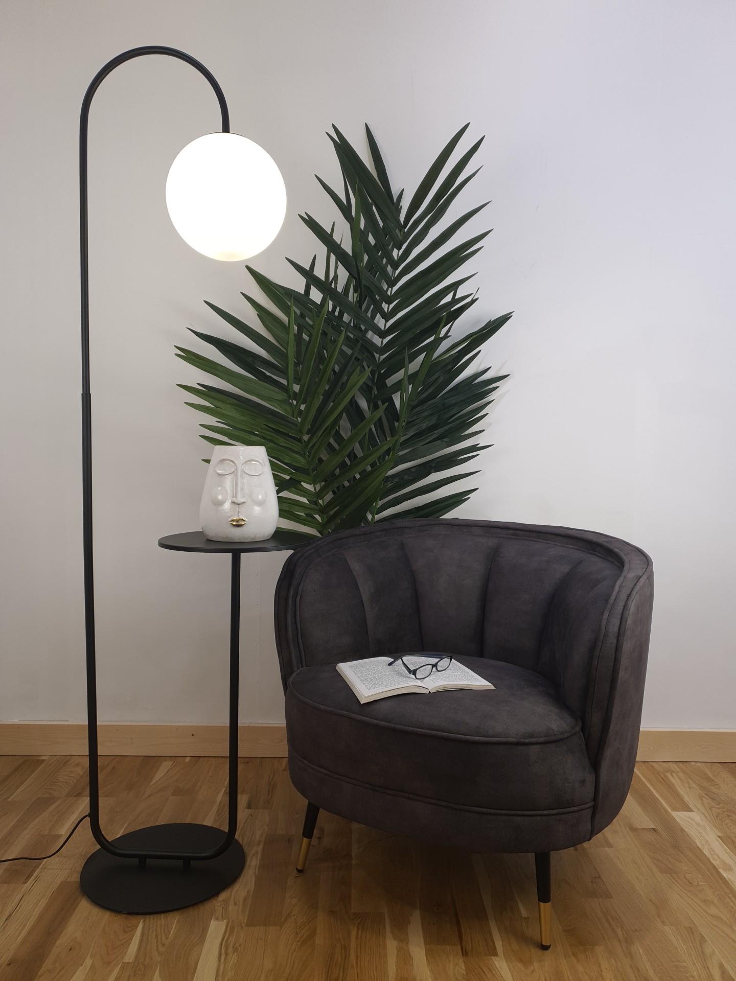 A floor lamp that double as a side table next to an armchair with a pot plant behind.