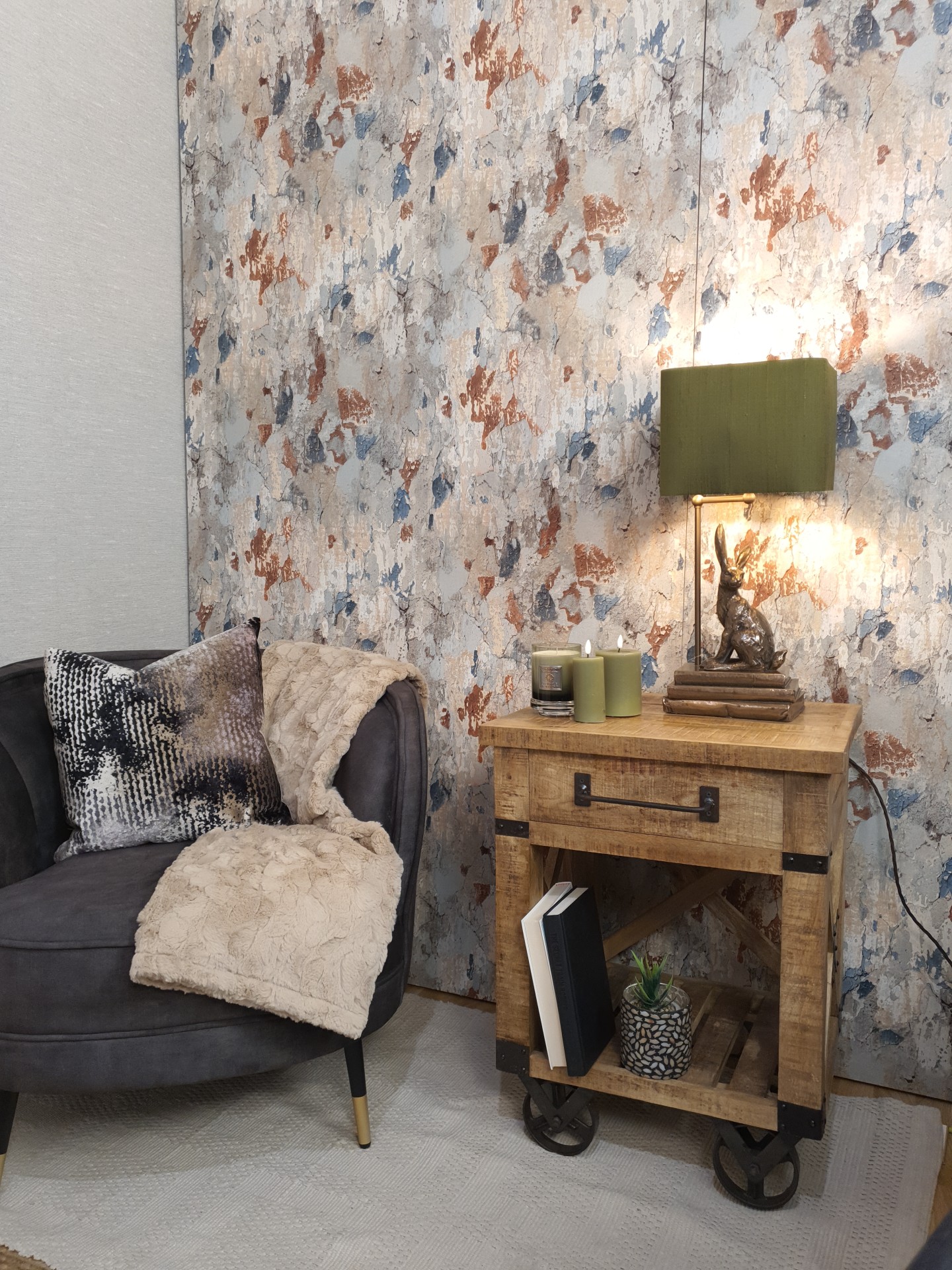 Hare shaped table lamp situated next to an armchair and in front of patterned wallpaper.