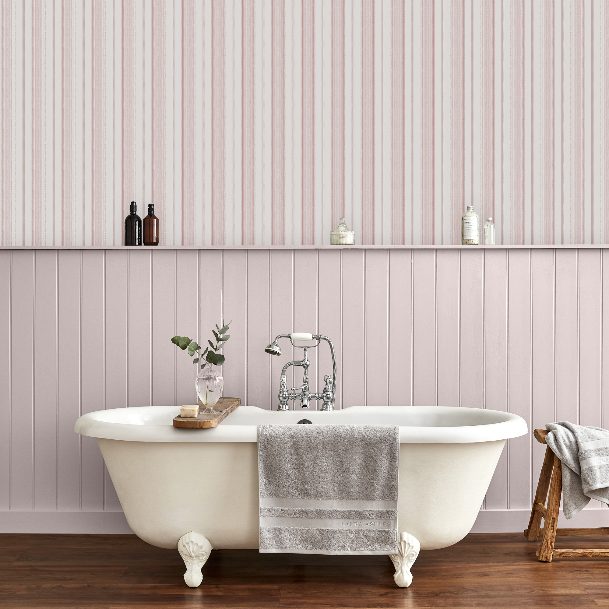 A bath tub in front on a half panelled wall with the other half in pink stripped wallpaper.