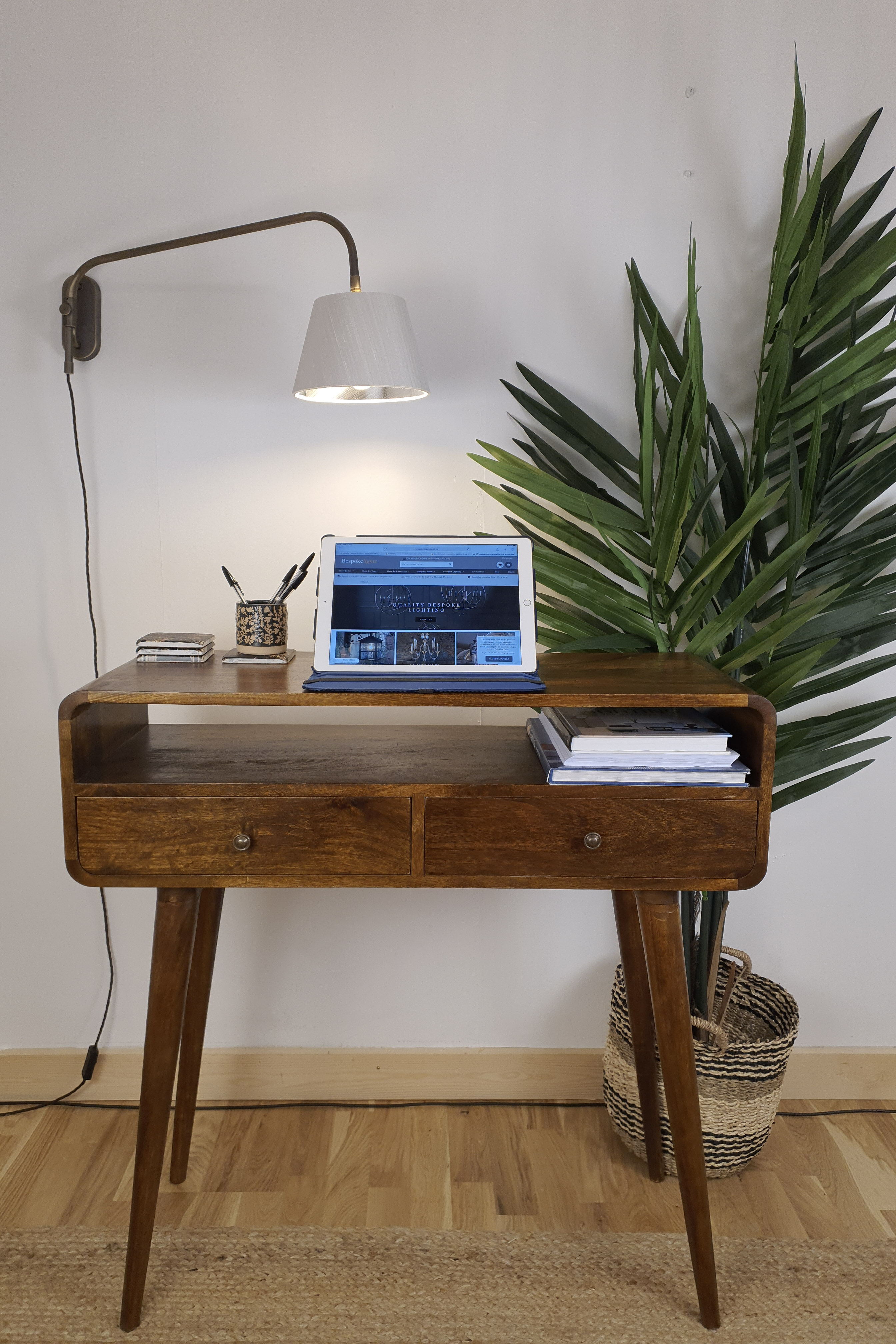 Office desk with a laptop and wall light with a large pot plant behind.