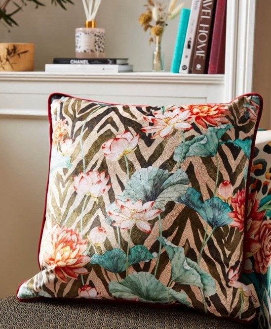 A floral and geometric pattered cushion on a sofa with a range of book behind.