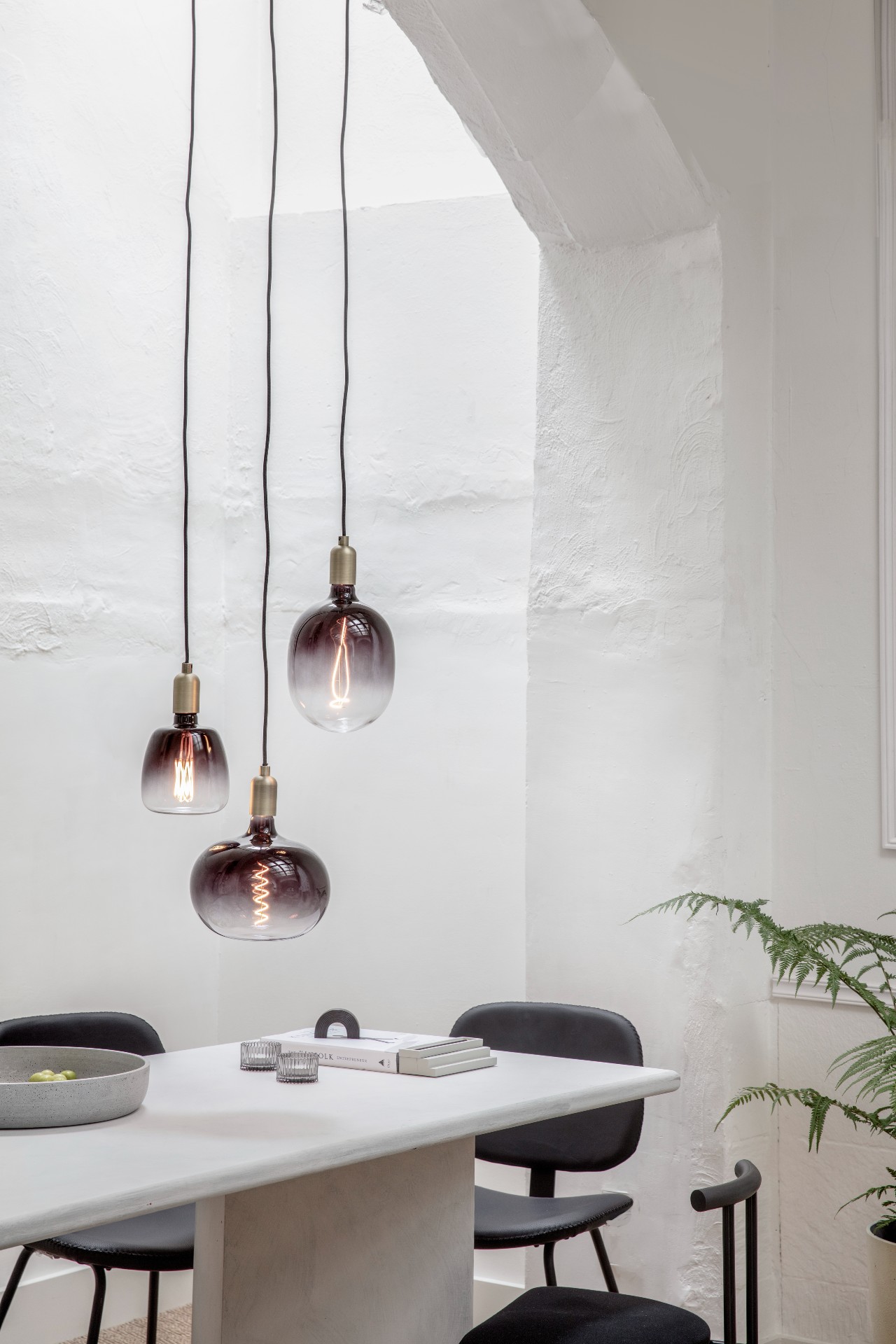 3 decorative and oversized bulbs hanging over a table and chairs.