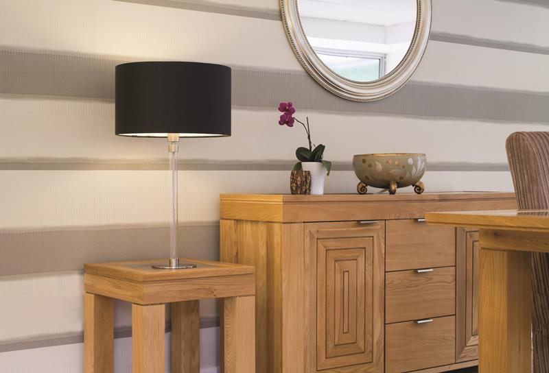 A table lamp on a coffee table next to a side board with a large oval mirror in the background.