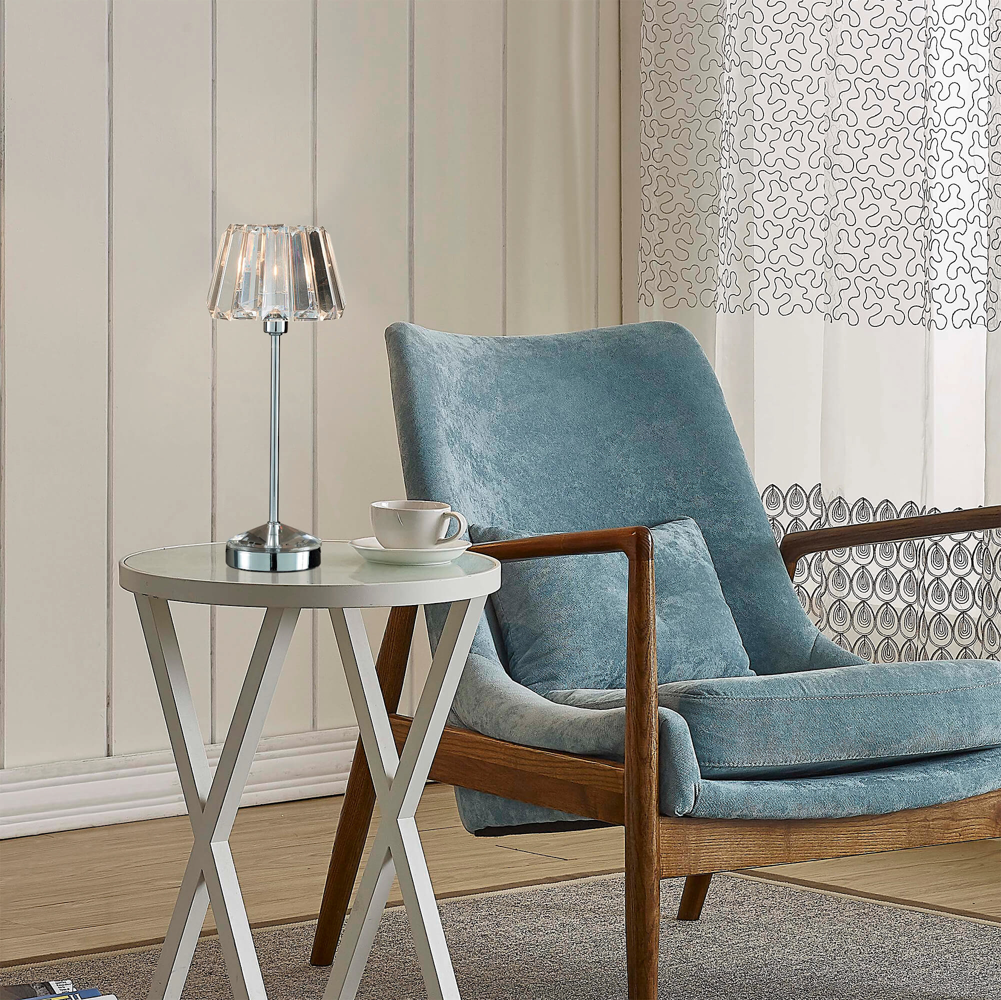 A blue arm chair next to a coffee table with a table lamp and coffee cup.