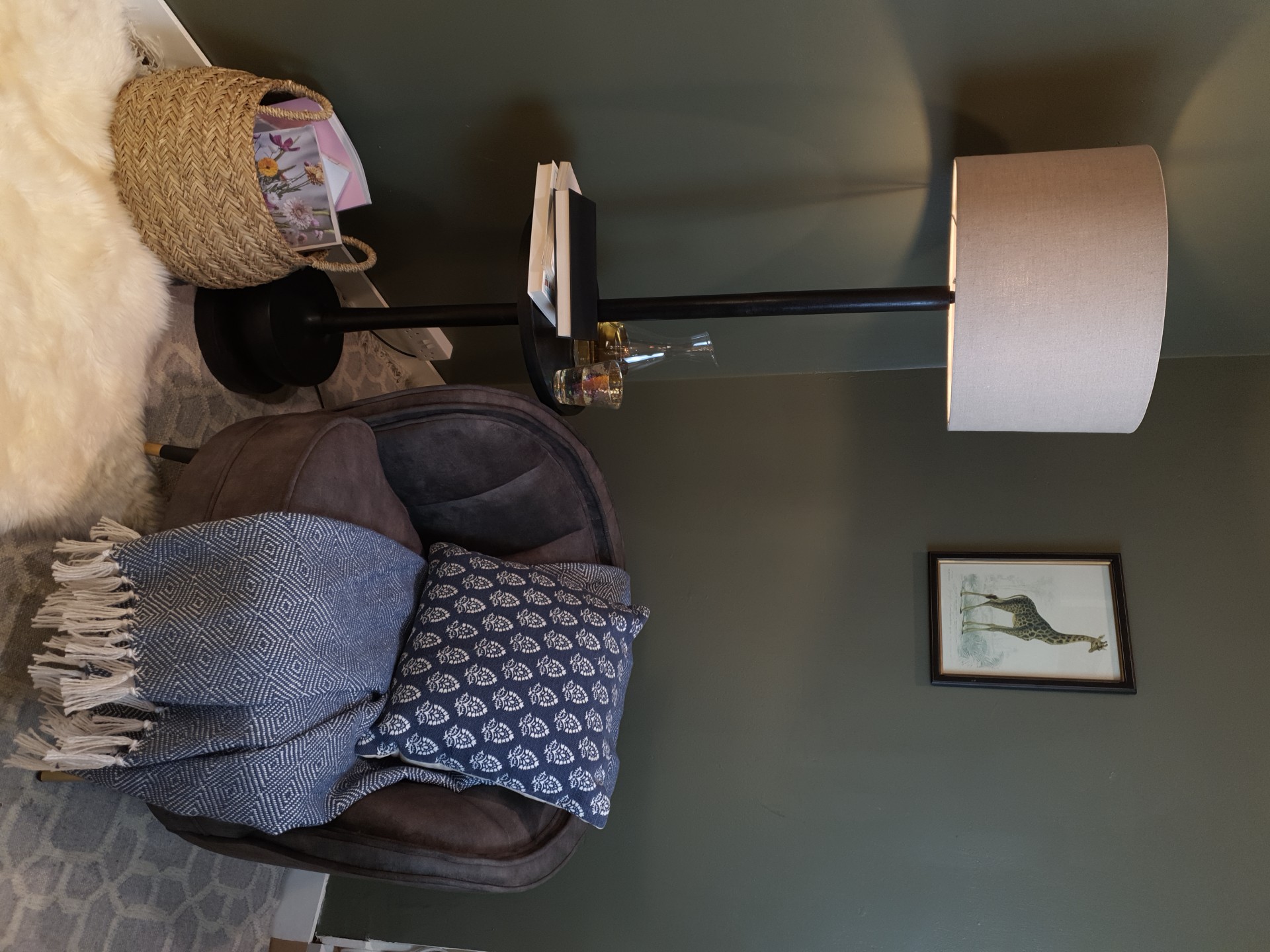 A floor lamp next to an arm chair, a giraffe image behind and a rattan basket and fluffy white rug.