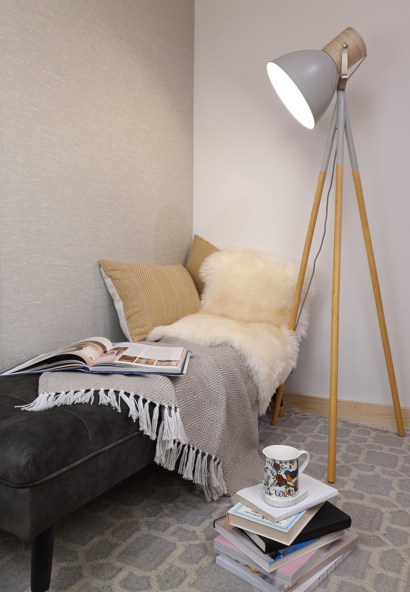 A selection of fluffy throws and pillows on a chaise longue with a floor lamp and pile of books next to it.