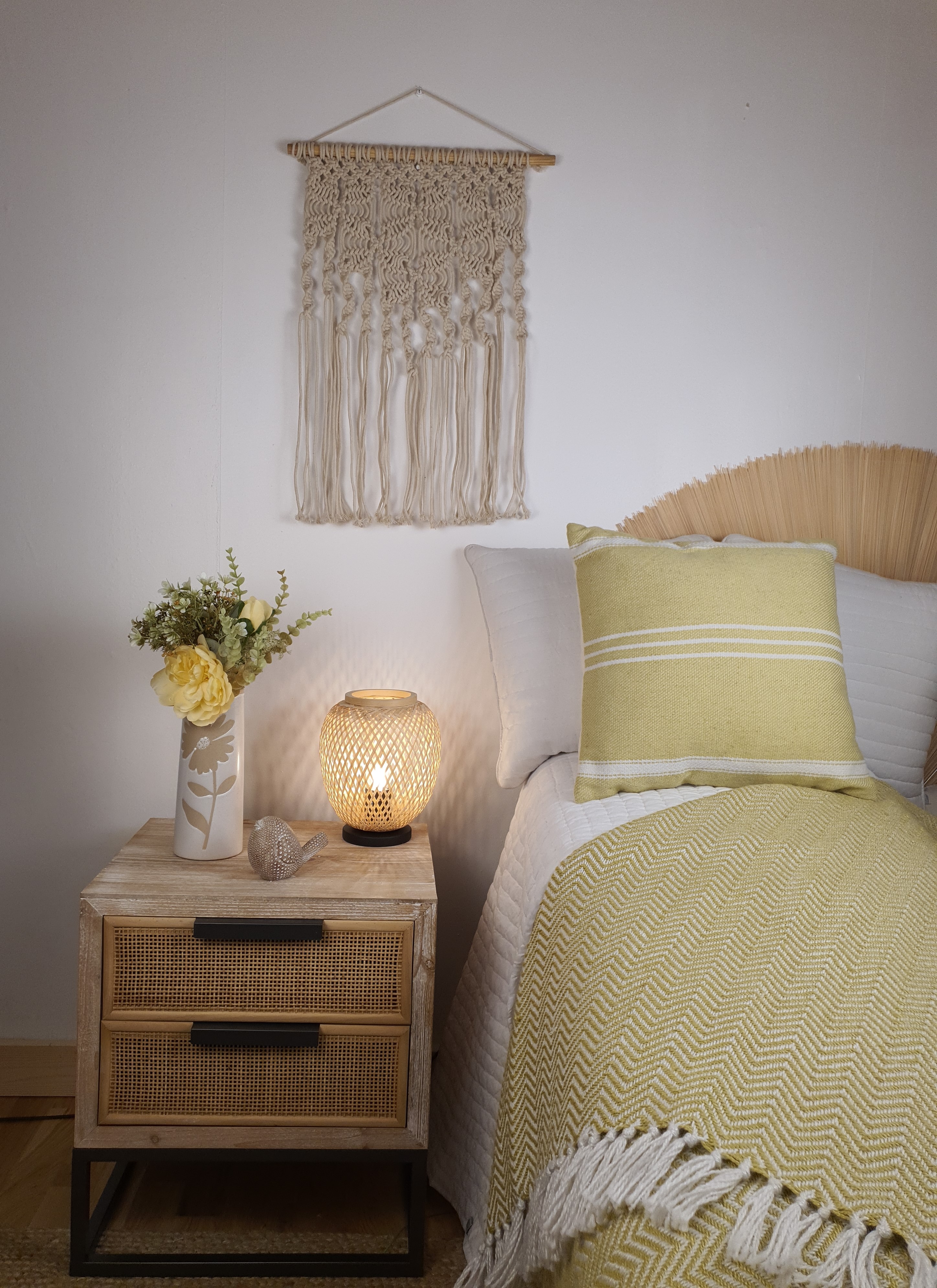 A table lamp on a bedside table next to a bed with wall art behind.