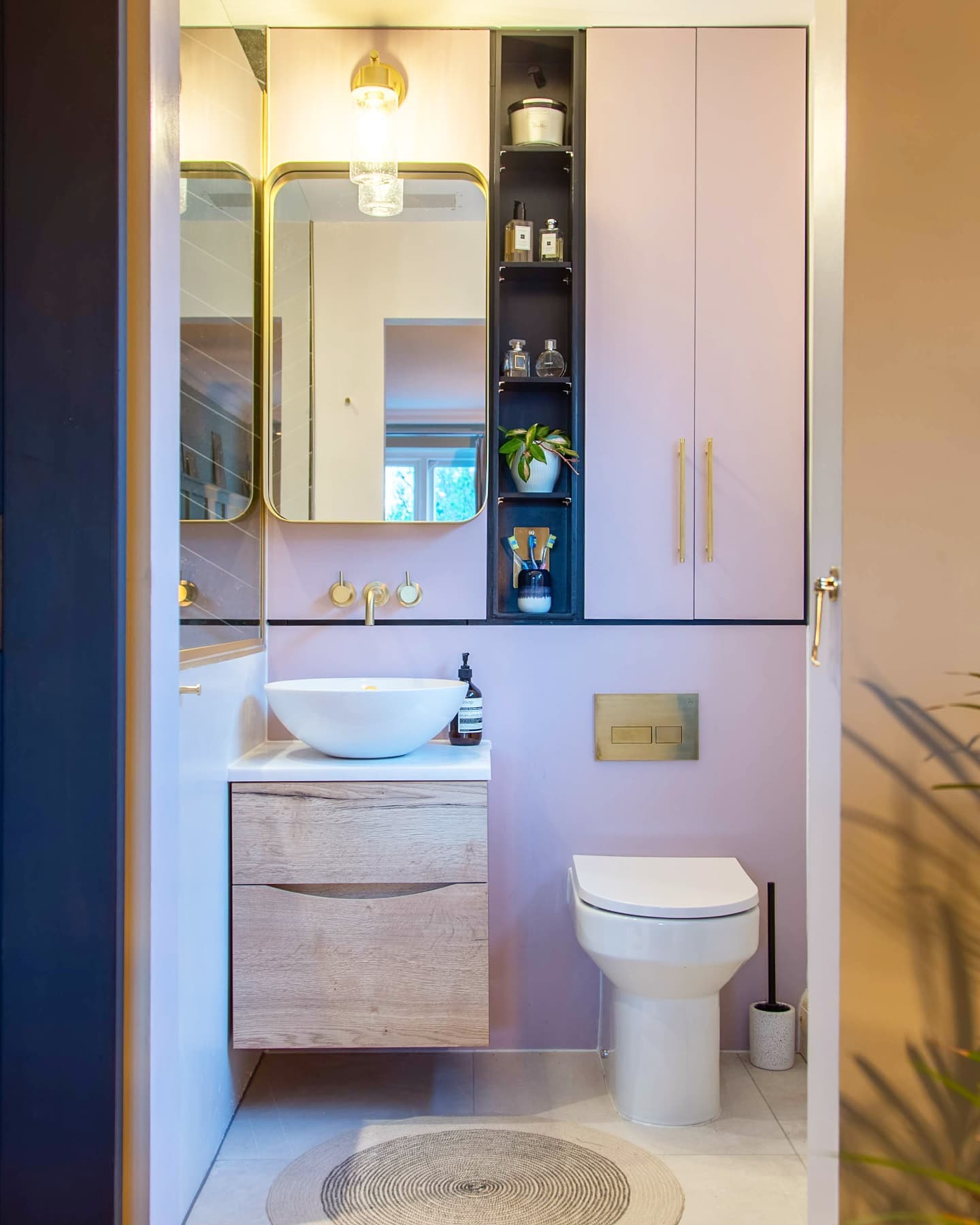 A bathroom setting, toilet, sink and cabinets with a mirror and wall light.