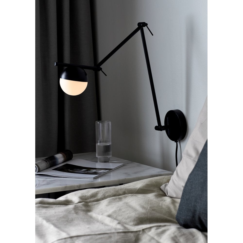 A black swing arm wall light next to a bed and placed over a bedside table.
