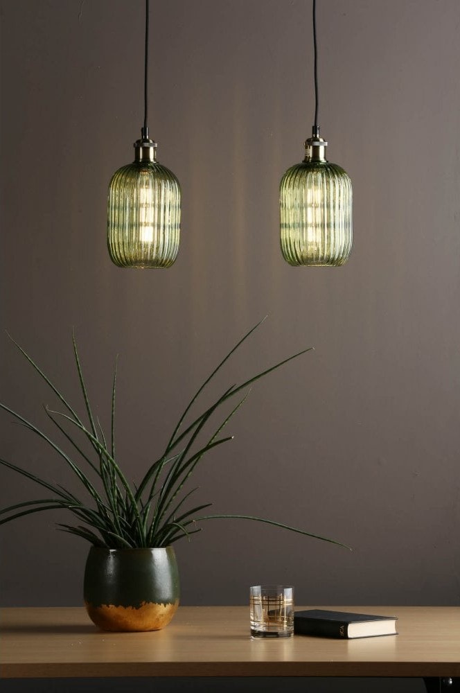 Two green glass hanging pendants over a pot plant with a book and glass next to it.