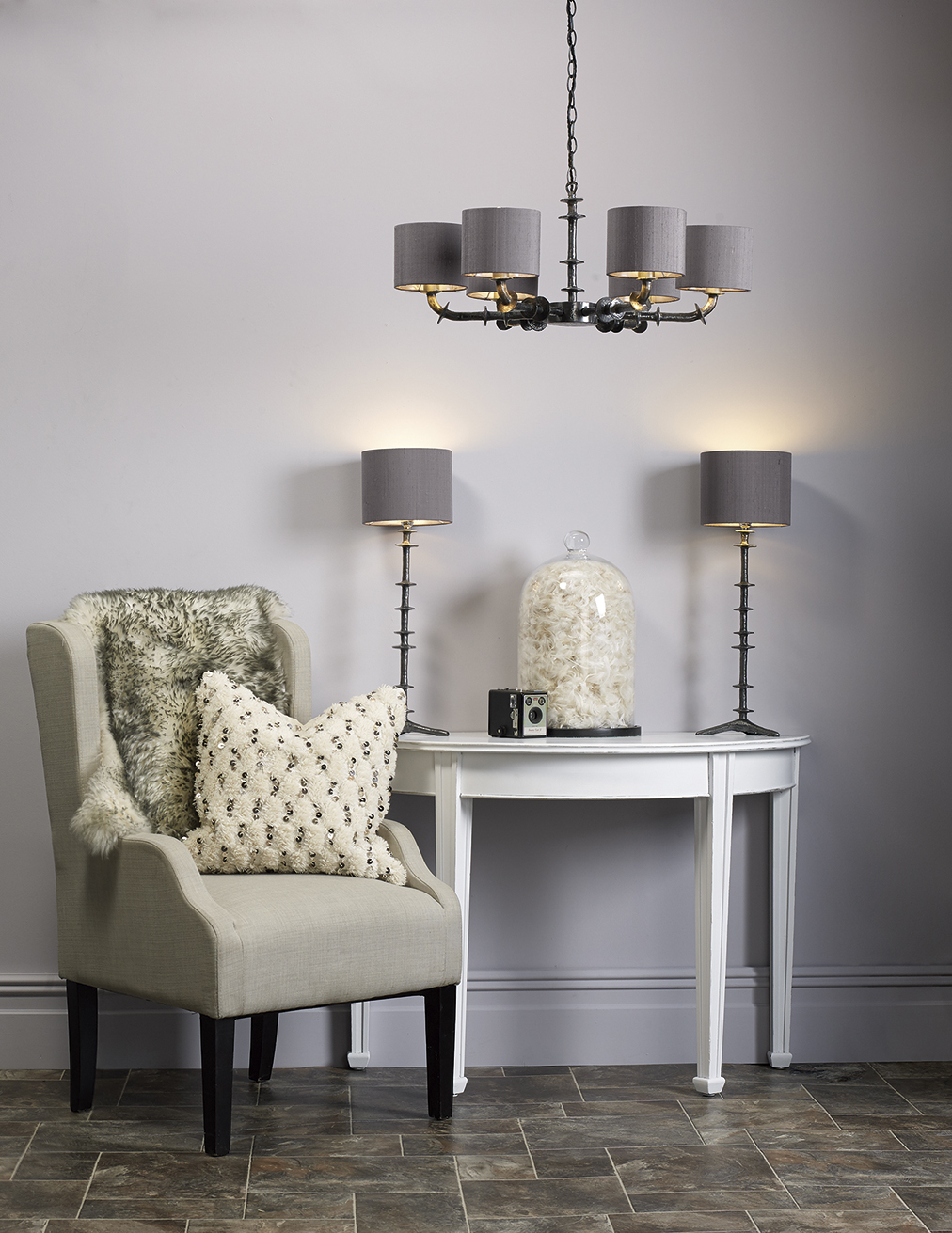 A 6 light pendant hangs over an armchair next to a table with 2 table lamps