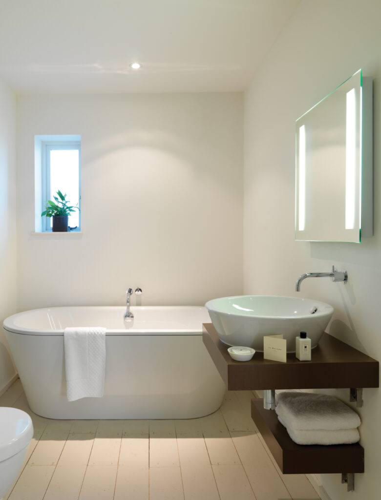 a modern fresh and bright white bathroom with recessed spotlights and back lit vanity mirror
