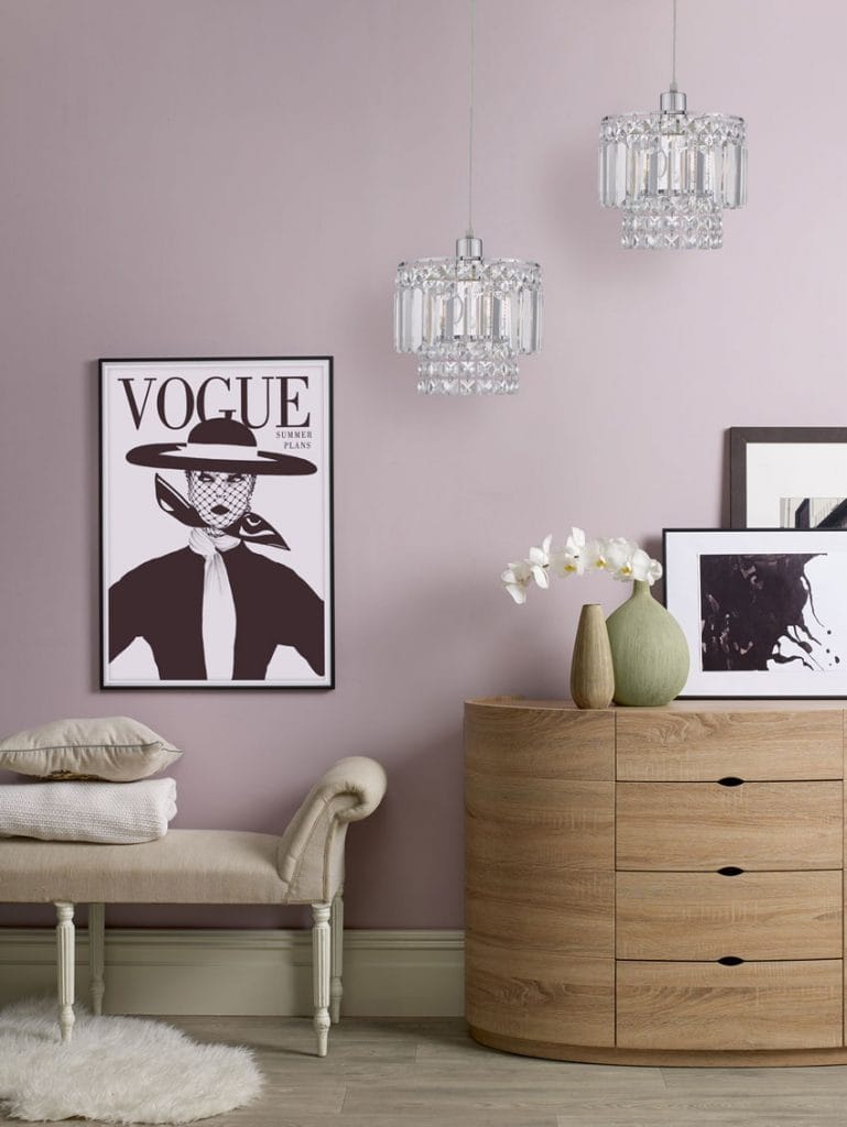 A large vogue poster with two glass pendants hanging over a wooden cabinet.