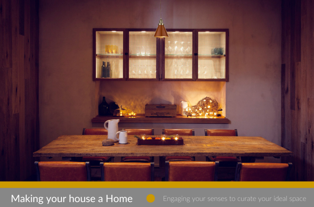 home dining room table with eight burnt orange chairs and vintage wooden table, white washed painted walls and 4 glass and wood cabnets in background with single brass light hanging above table.