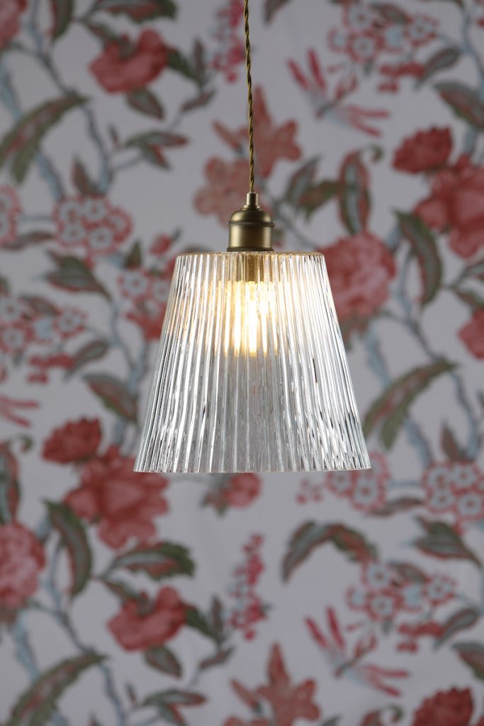 Glass fluted desgin ceiling light with brass finish, with 80s inspired clear ridges, backdrop of a red, white and green floral wallpaper