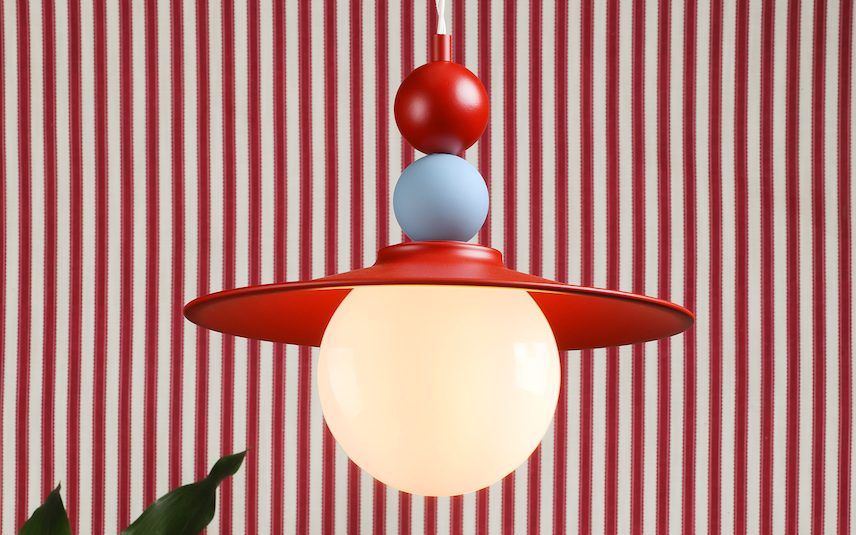 80s inspired ceiling light in red and blue with a white globe bulb, backdrop with 80's inspured red and white striped wallpaper