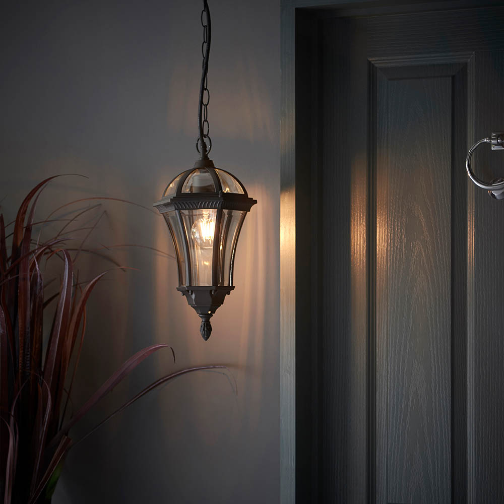 A dark hallway with a black and glass hanging lantern in a medieval, gothic style with a warm glow emanating from it