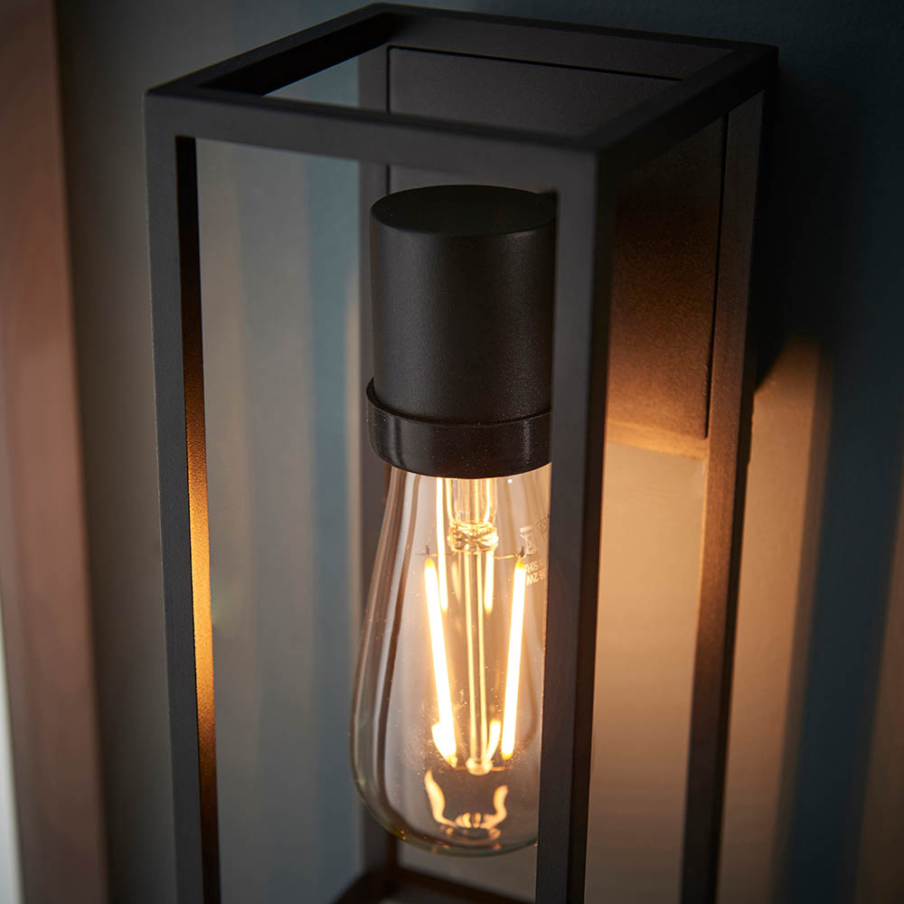 A modern wall mounted light fitting that encapsulates a warm, gothic feel with black metal frame and amber bulb