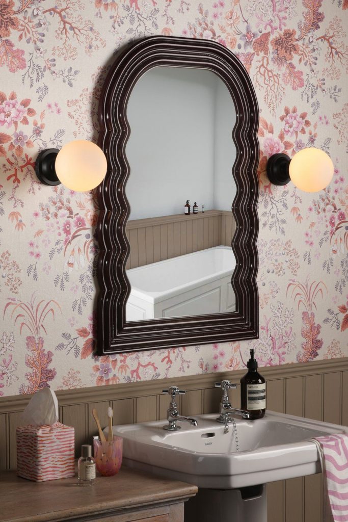 A pair of black, wall mounted, warm white, globe style bathrooms lights mounted either side of a mirror in a period property with pink decor