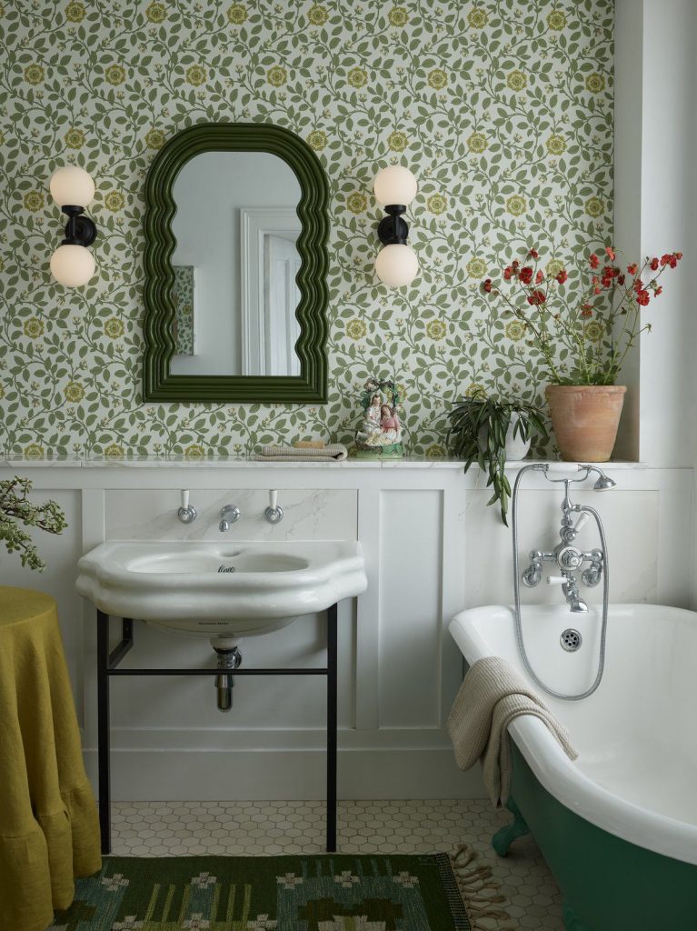 A pair of wall mounted, warm white, globe style bathrooms lights mounted either side of a mirror in a period property with green, floral decor