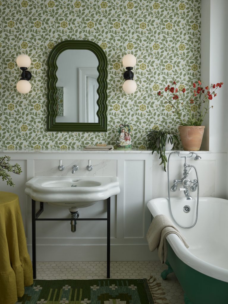 a green floral Victorian style bathroom with traditional features like roll top bath and freestanding wink with modern black and opal glass wall lights next to a mirror
