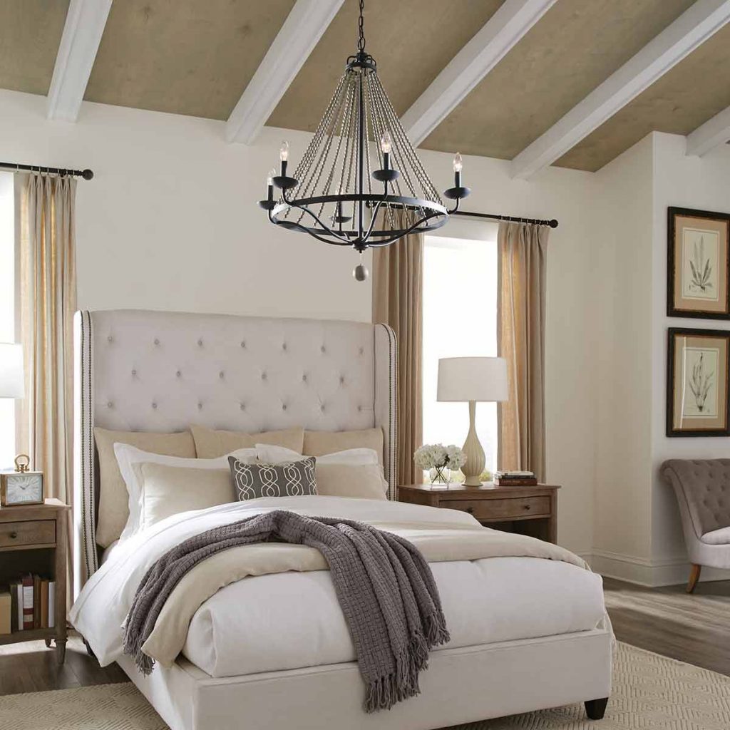 a black chandelier with candle effect bulbs in a gothic or medieval style hanging in a bedroom