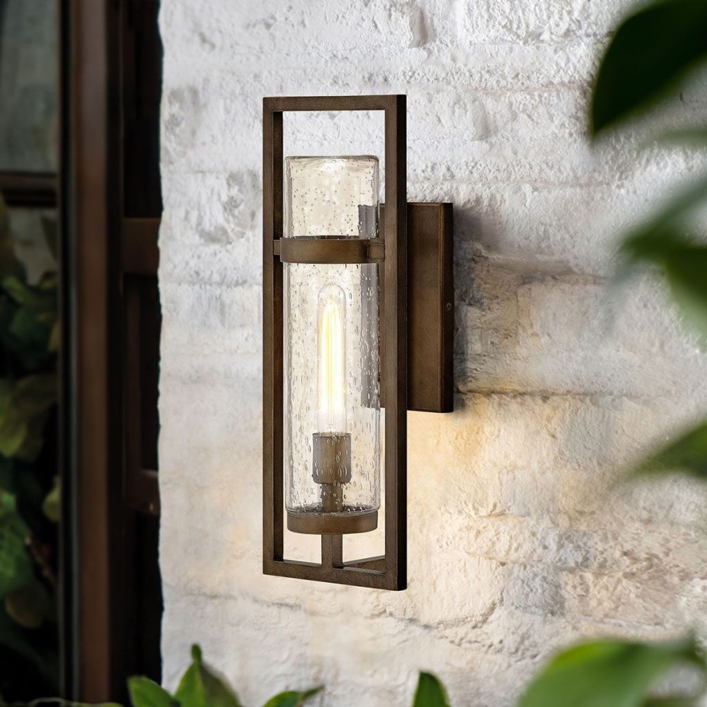 An aged bronze effect wall light fitting with a glass column shade and warm bulb that would be suited to a medieval style bathroom in a period property