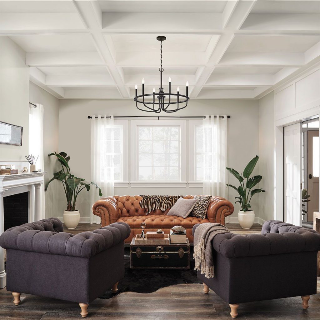 A large, black, wrought iron medieval style chandelier with candle style bulbs suspended over a chesterfield sofa and arm chairs in a living room within a period property