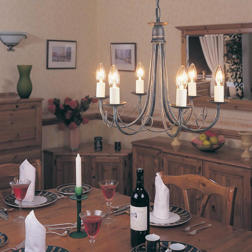 A medieval style chandelier with candle style light bulbs hanging low over a rustic dining table in a period home