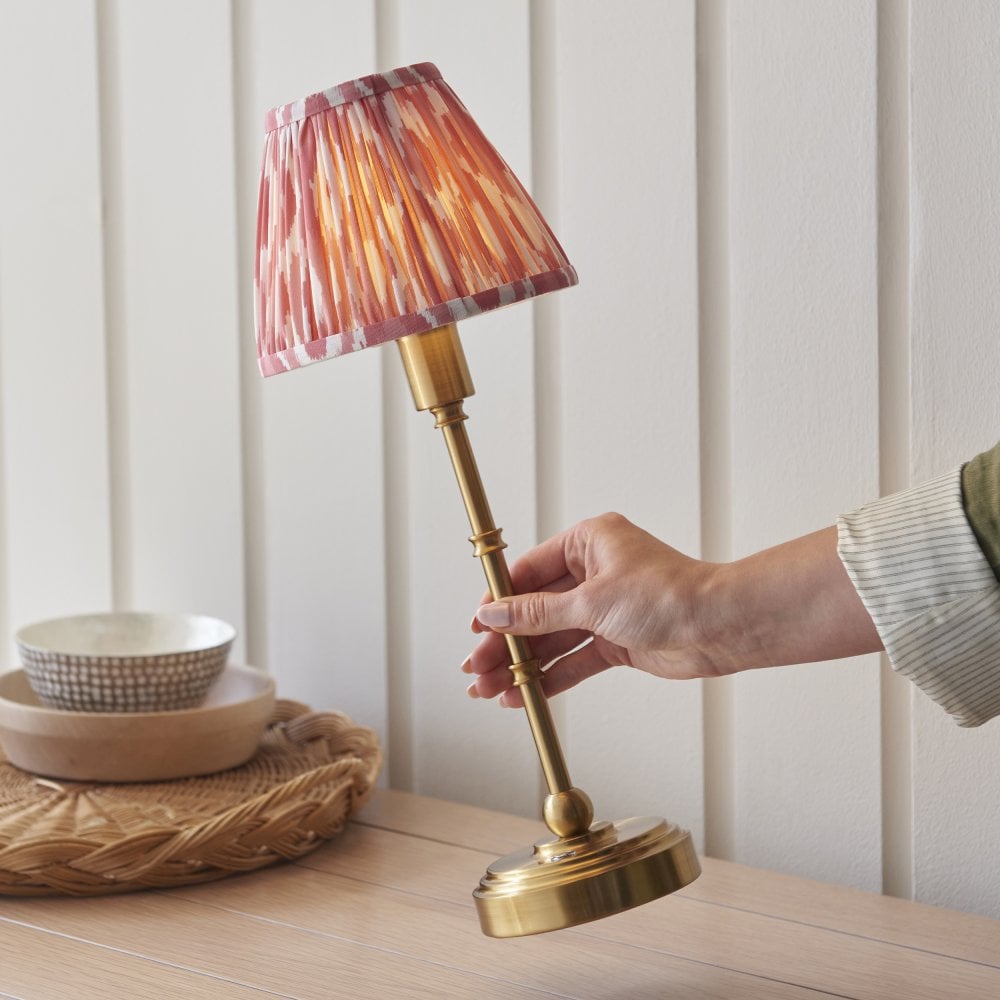 a brass rechargeable table lamp with pink zig zag patterned shade