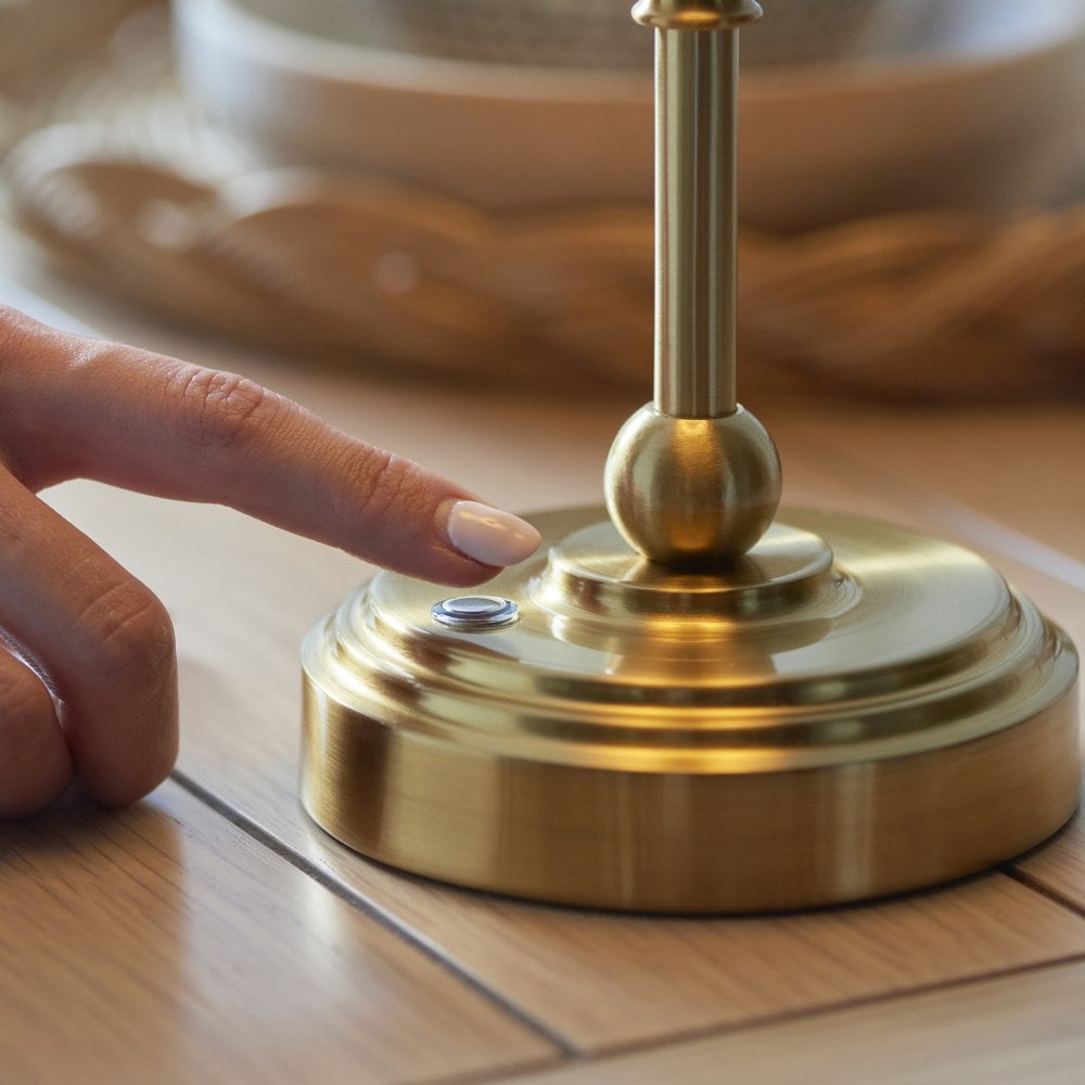 A person pressing a button on the base of a brass table lamp