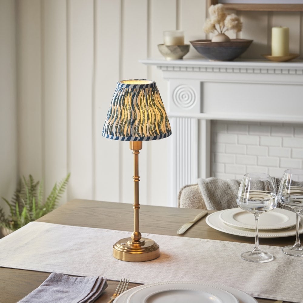 A brass lamp with blue and cream patterned lampshade on a dining table
