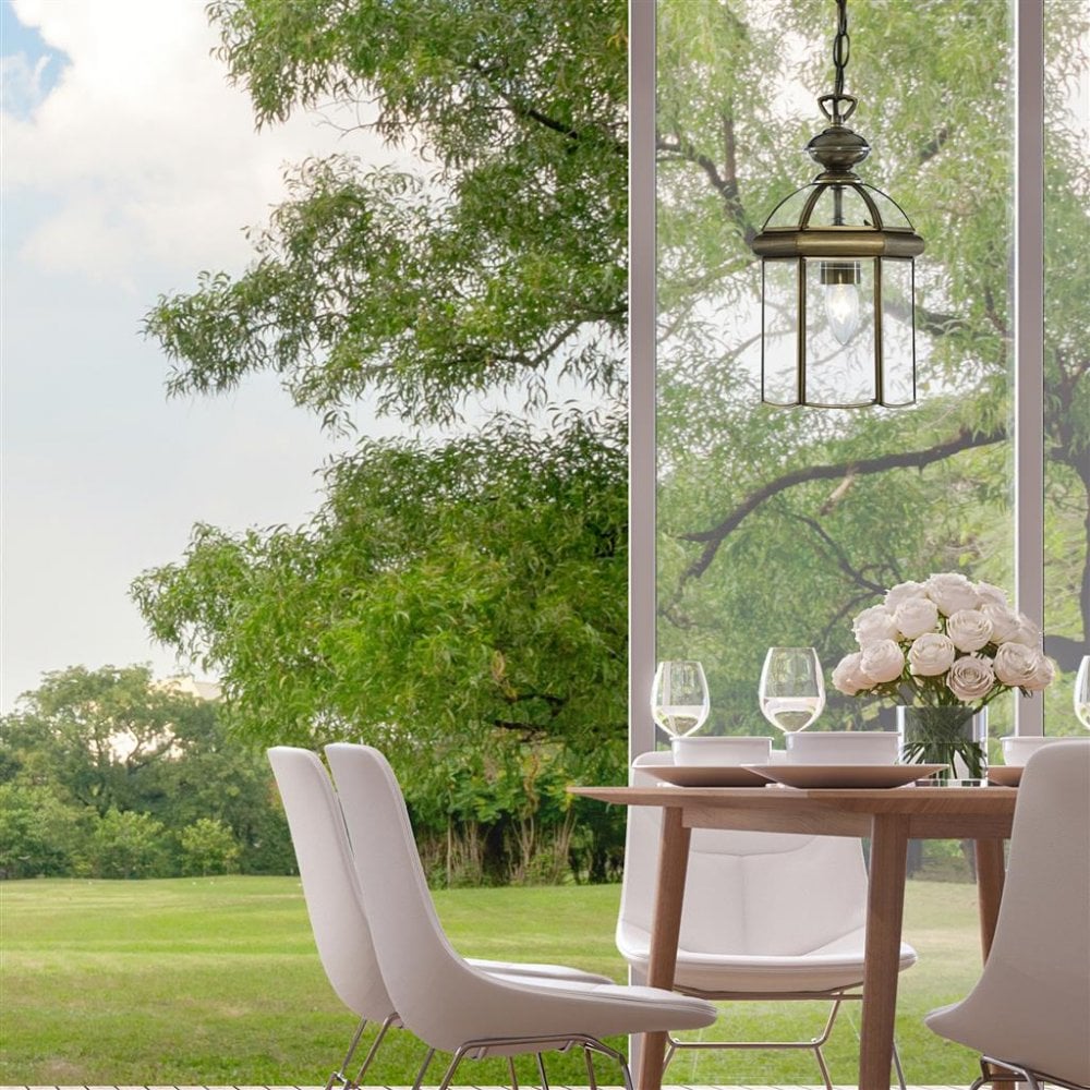 An aged brass pendant lantern in a regency style hanging over a dining table in a open kitchen door by a garden