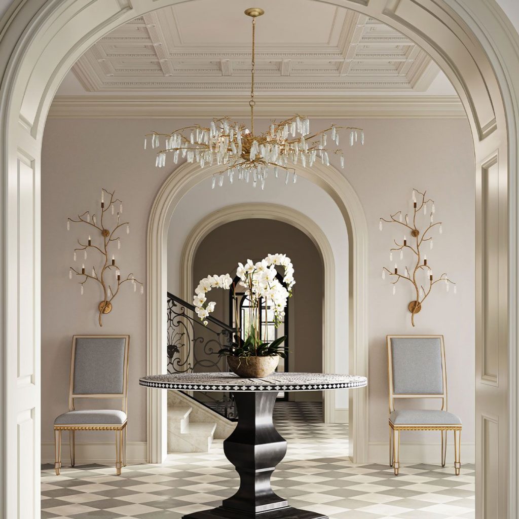 large ornate gold and glass modern chandelier fitting with matching wall lights in a grand country house entrance hallway with a table featuring a white orchid.