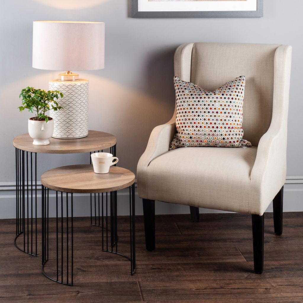 a living room with neutral arm chair and next of table with cream lamp and plant