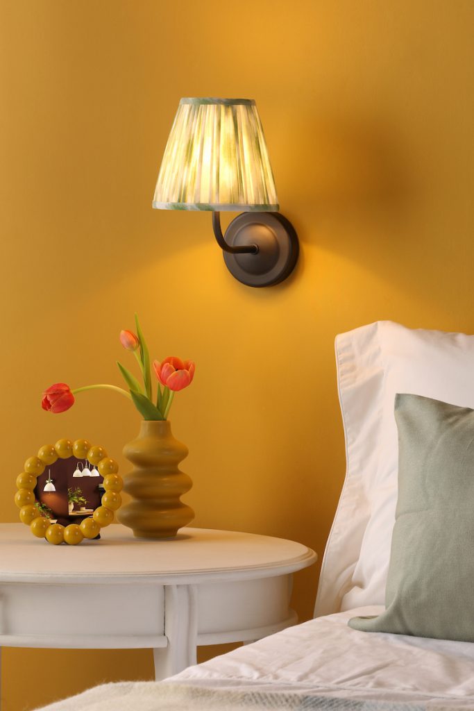 a rechargeable wall light in a matt black finish and green patterned shade beside a bed
