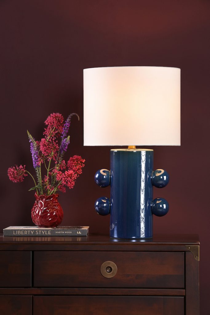 a modern blue decorative table lamp with cream drum shade on a wooden sideboard