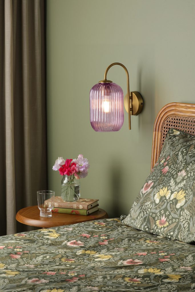 a brass wall light with decorative pink ribbed glass shade in a green bedroom