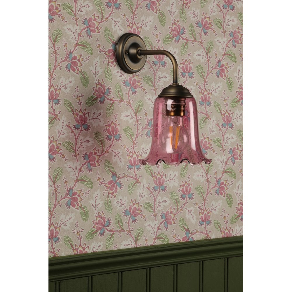an aged brass wall light with pick glass shade in a vintage style