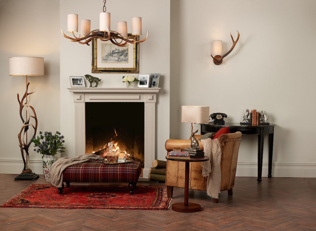 a warm and inviting living room with fireplace and mantlepiece with an antler floor lamp, wall light and chandelier with cream linen shades