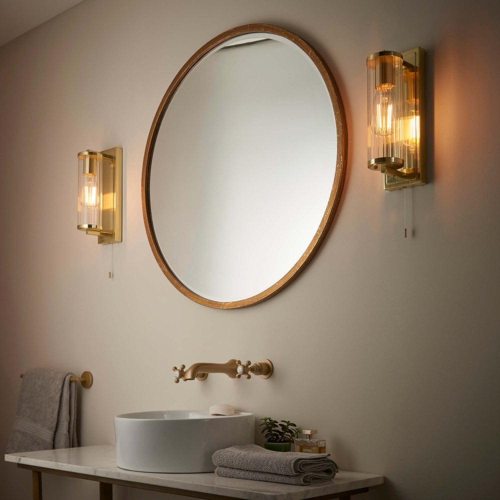 modern brass column wall lights with ribbed glass paired with a round brass mirror